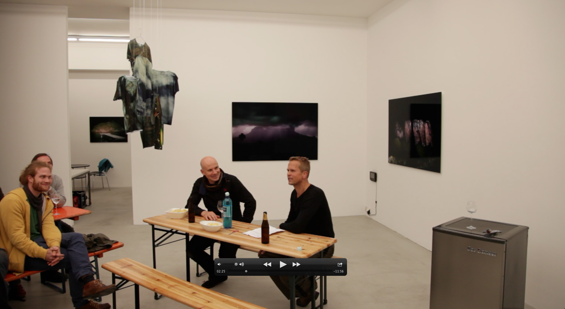 Visitors seated at beer-garden tables during a gallery talk at Galerie Heike Strelow, with the Das Eismeer fridge piece visible, Frankfurt, 2012